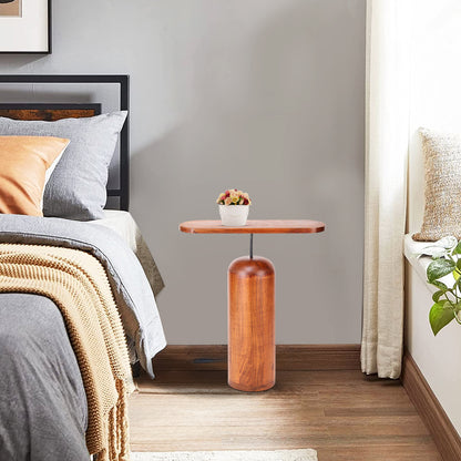 ARDERA wooden side table with a cylindrical wooden base and rectangular wooden top, placed in a cozy bedroom setting. The table features a small decorative plant on top, blending beautifully with the neutral tones of the bedding and the room’s natural lighting