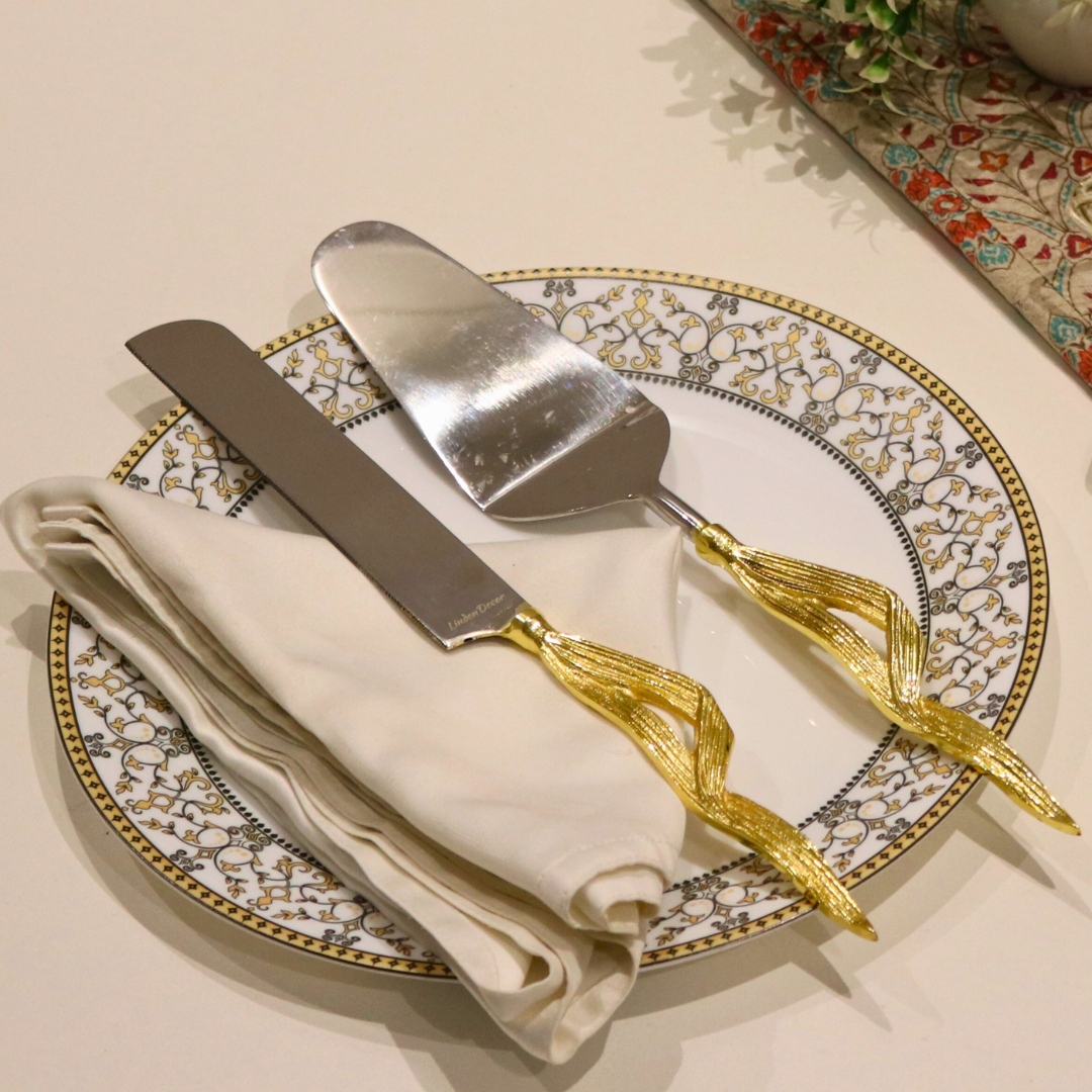 Golden Maize Leaf Cake Server Set with stainless steel blades and maize leaf-inspired handles, elegantly placed on a decorative plate with a slice of chocolate cake